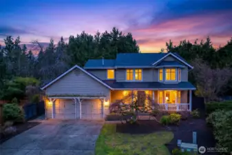 Arrive to a warm, welcoming presence as the home glows at dusk, set back at the end of a quiet cul de sac. The covered front porch and mature landscaping create a calm first impression, paired with the confidence of a newer roof (2024) and quality windows.