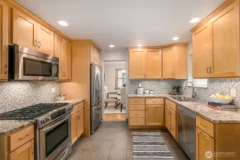 The kitchen has been updated with shaker cabinets, slab granite counter, tile back splash and stainless appliances.  Notice the gas cook top and tile floors.