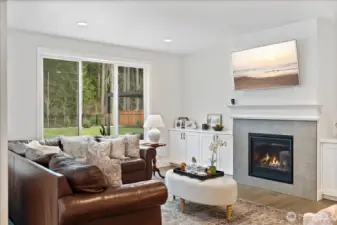 Bright family room next to the kitchen with a gas fireplace, custom mantle, and expansive windows framing the backyard and peaceful greenbelt views.