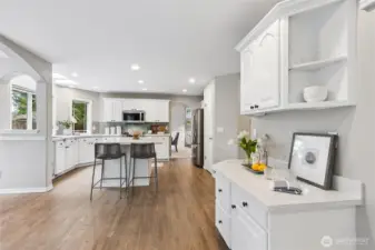 A built-in desk area with additional cabinets provides a convenient and useful workspace while upper cabinets continue the crown molding detail for a cohesive look. The desk area is finished with quartz countertops and backsplash blending style with functionality.