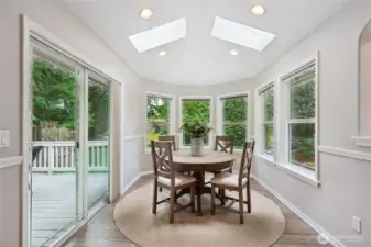 The kitchen adjoins a spacious casual dining area, highlighted by curved panoramic windows that overlook the backyard and skylights above that fill the space with natural light. A sliding glass door opens to the 246sf deck, creating a seamless transition to outdoor living and entertaining.