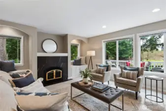 A gas fireplace anchors the room, complete with a large niche above and built in cabinetry alongside. A wall of windows overlooks the back deck and yard, filling the space with natural light and enhancing the connection to the outdoors.