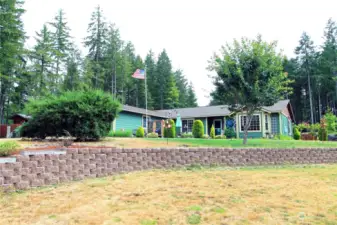 From the Northwest corner of the front yard looking Southeast. Serene setting with mature landscape and outdoor seating on the patio offering captivating views of the Olympic Mountains and Hood Canal.