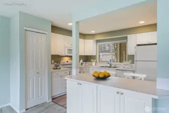 Kitchen with eating space seen from the dining room/living room. Pantry to left of kitchen counter with more storage below breakfast bar.
