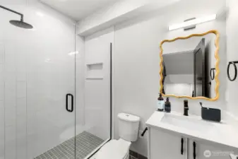 Primary bath, features glass door entry & full tile surround. Continues luxury finishes, quartz countertops, & rainfall showerhead. This image is virtually staged.
