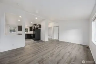 Looking across the living room, the oversized cutout into the kitchen does exactly what good design should, it lets light travel, keeps conversation flowing, and makes the space feel bigger without removing walls entirely. The vaulted ceiling amplifies the effect, while the hallway to the bedrooms stays tucked away. With sunlight pouring in from the front window, this room feels bright, balanced, and easy to live in.