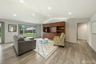 Notice the vaulted ceilings that add depth and openness to the space, complemented by a large picture window with automated blinds for light control and privacy. You'll find the primary suite, utility room, two bedrooms, and the main bathroom down the hall you see in the right of this photo.