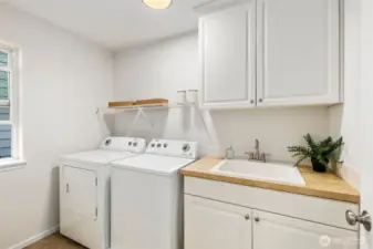 Upstairs near the bedrooms, this spacious laundry room features a Whirlpool washer and dryer (2014), a sink for hand washing, and abundant cabinetry for storage. New LVP flooring adds durability and style, while a large window fills the room with natural light.