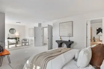 Another view of the expansive primary suite shows double-door entry and direct access to the en suite bath. The sitting area feels like its own peaceful lounge space — beautifully lit by natural sunlight and enhanced by fresh, neutral tones.