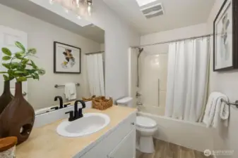 This fresh and functional full bath has been thoughtfully updated with new LVP flooring, a sleek new toilet, modern black faucet, stylish new vanity lights, and a luxurious new handheld shower head. A skylight fills the space with natural light, while the 2019-installed fan keeps things comfortable—making this bathroom a bright and practical addition to the home.