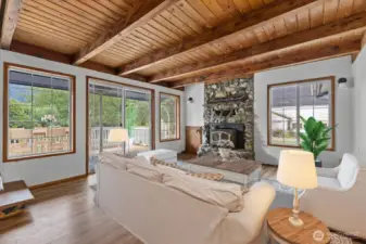 The Family room w/ tongue & groove ceilings, lg beams, woodstove, laminate flooring & a slider to the back deck. Virtually Stage.