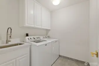 Laundry room on the mail floor with a new tiled floor, quartz utility sink and white cabinets.
