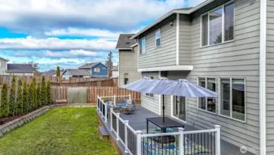 Backyard with full length composite deck with rails and 3 separate sets of stairs. Small retaining wall borders the yard and offers flowerbed space.