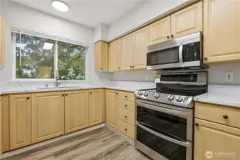 Kitchen features stainless steel appliances, granite countertops, a high-top breakfast bar, and bright light-tone cabinetry.