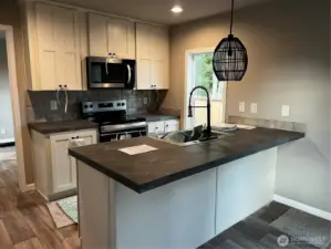 Kitchen with eat in bar and unique pendent light. All appliances come with home.