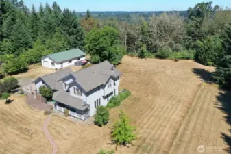 Aerial shot showcasing the beautifully maintained home, detached shop, and expansive fenced acreage. Surrounded by mature trees and privacy with room to roam, garden, or explore.