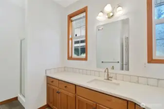 Bright and clean lower bathroom with tile backsplash, and a large windows for natural light. The space features luxury vinyl plank flooring and a separate toilet area for added privacy.
