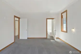 Another angle of the primary suite showcasing wall sconces, dual windows, and access to the en-suite bath. Spacious and serene.