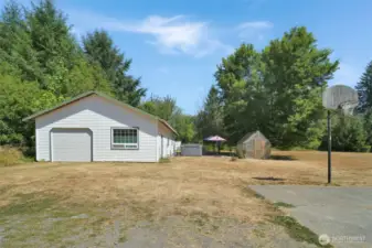 The detached shop sits next to a patio area with hot tub/swim spa, a walk-in greenhouse, and open yard space. Perfect for gardeners and hobbyists alike.