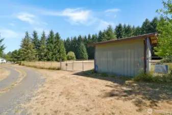 Gravel drive leads to a large fenced pasture with gated entry. A small outbuilding sits at the entrance, horse ready shed indicating current or prior use as an animal-friendly space.