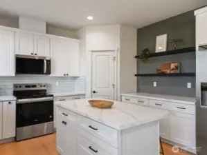 Island in Chef's kitchen with seating. Stainless Appliances include the Fridge.  Additional Counter & Cabinet Space with floating shelves is an added plus.