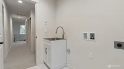 2nd floor laundry room has utility sink with cabinet and tile flooring.