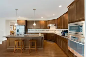 A closer look at the gourmet kitchen shows abundant counter space, stylish tile backsplash, and pendant lighting that highlights the oversized island. Double ovens, gas range, and a deep farmhouse-style sink make this kitchen both functional and beautiful.