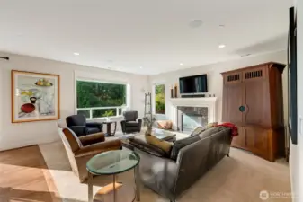 Spacious and inviting living room with large picture windows that frame lush greenery outside. The focal point is the gas fireplace with elegant tile surround and a custom mantel, ideal for cozy evenings or entertaining guests in comfort.
