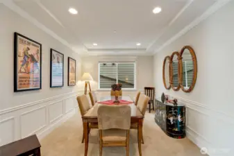 Elegant formal dining room featuring classic wainscoting, tray ceiling, and soft recessed lighting. The space easily accommodates a full dining set, offering the perfect spot for family gatherings or dinner parties in a warm, refined atmosphere.