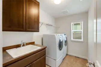 Dedicated upstairs laundry room with front-loading washer and dryer, deep utility sink, and upper cabinetry for storage. Conveniently located with space for folding and organization.