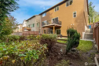 Rear elevation view highlighting the covered patio, upper deck, and fully fenced yard surrounded by mature landscaping for privacy.