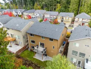 Aerial view from behind the home showing the fenced backyard, outdoor living spaces, and greenbelt backdrop providing privacy and natural scenery.