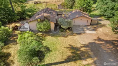 Front side of home, w/ large deck,  14ft picture windows, + 2 car shop/garage and barn/fenced fields in the background