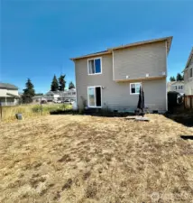 Rear view of the home with a partially fenced yard and community parcel next door.