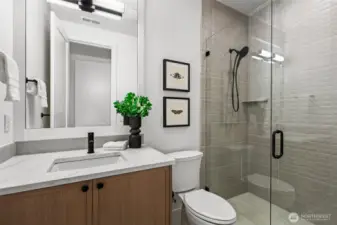 Main floor guest en suite bathroom. Step-in shower with frameless glass doors, floor-to-ceiling dimensional tile, and a shampoo shelf.