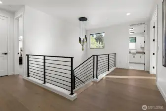 Airy upper level landing in engineered wide-plank oak hardwoods and open stairwell. In this photo, an ensuite bedroom is on the left, hallway linen closet, laundry room straight ahead, and the French door opening on the right leads to the primary bedroom.