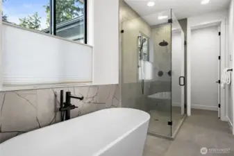 Large format porcelain wall tiles wrap the lower tub wall and extend from floor-to-ceiling in the walk-in shower. Two shower heads, one with an adjustable arm.