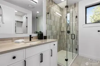 Upper level ensuite bathroom. Large vanity with slab counters, framed mirror, shower with frameless glass shower doors, a shampoo shelf, and a walk-in closet.