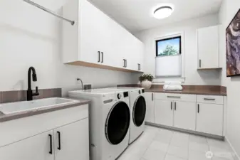 Laundry room lined with cabinets, slab countertops, large utility sink with pull-out faucet, LG® washer and dryer, and a hanging bar.