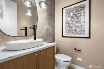 Powder room with accent wallpaper, vessel sink, hanging decorative pendants, slab quartz countertops, and a framed mirror.