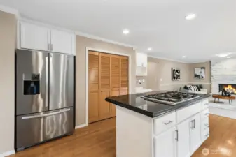 Another view showing the fridge, pantry and island with storage and gas cooktop on top.