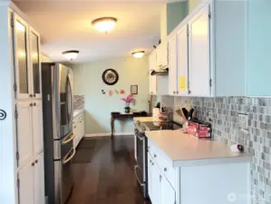 Opposite View of the Huge Walk Through Kitchen with Tile Back Splash, White Cabinets, Stainless Appliances, Newer Paint and  Hard Wood Flooring Looking at the Eating Area.