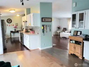 An Over All View from the Dining Room looking at the Huge Walk Through Kitchen with Tile Back Splash, White Cabinets, Stainless Appliances, Newer Paint, Hard Wood Flooring and Living Room.