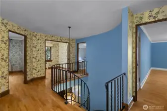 Curved walls, iron railing, and vintage character define this upstairs hall, a reflection of the home’s enduring craftsmanship.