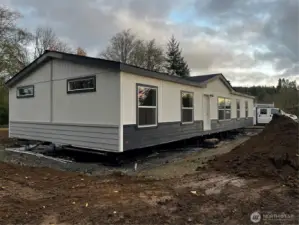 Front of Manufactured home. Front stairs/deck and sidewalk to come. Builder also has plans for concrete curbing, gravel parking pad and hydroseeding soon. Paint still needs finalized on ends of manufactured home.
