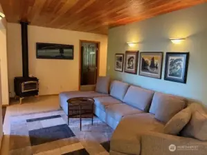 Living room area with tile flooring, beadboard wood ceiling, and freestanding propane stove.