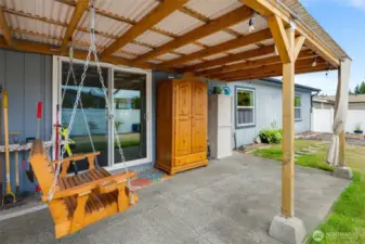 Covered patio with outdoor curtains, swing and TV setup invites you to unwind and enjoy the peaceful yard.