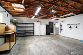 Garage offers a work bench, shelving, white freezer, black fridge and extra space for hobbies, tools, or storage needs.