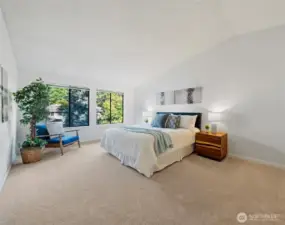 The spacious and serene Primary Suite offers a retreat, featuring vaulted ceilings and large windows that fill the room with natural light and views of the lush surroundings.