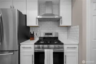 Gas range, stainless hood, and subway tile backsplash bring clean, modern style to the kitchen.
